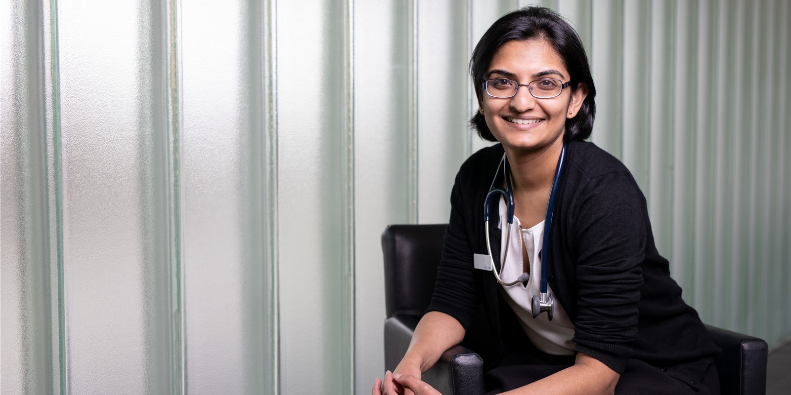 Dr Sumitha Bhaskaran, Head of General Medicine Monash Medical Centre sits on a chair, smiling with her hands clasped together.