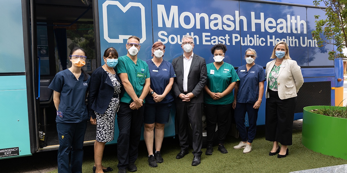 Victorian Minister for Health, the Hon. Martin Foley MP stands in front of the Monash Health Vaccination Bus surrounded by Monash Health employees on either side of him.