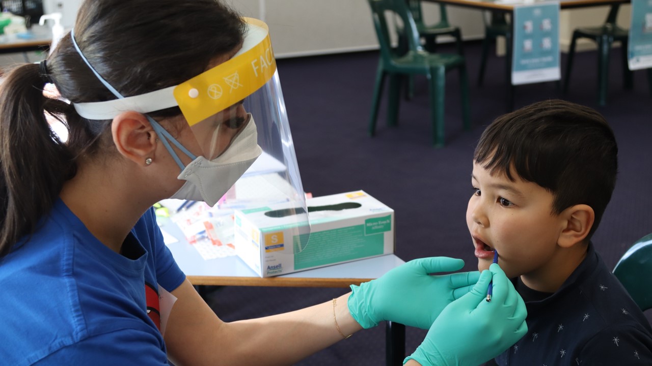 An oral health educator inspects 6-year-old Danial's teeth for any dental problems. She holds a small mirror inside his mouth to inspect his teeth.