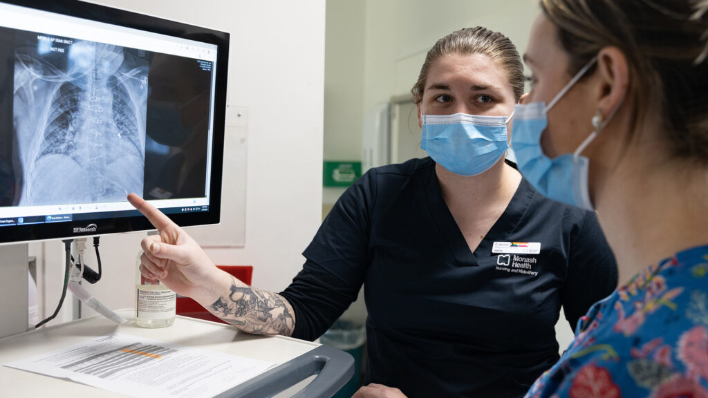 A student nurse points to a scan on a screen while looking at Aisling.