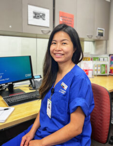 Social Worker Ling Toh sitting at a computer turning to smile at the camera.