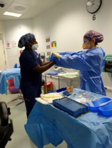 An operating theatre nurse helping a colleague put on surgical gloves.