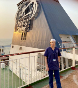 A nurse in scrubs standing on the deck of a Mercy Ships vessel.