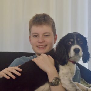An 18-year-old man with short brown hair hugging his dog smiles for a photograph.