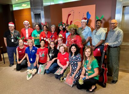 A group of carolers wearing festive colours and holding song sheets pose for a group photo.