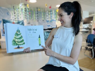 A woman reading a picture book to young patients points at the illustrations.