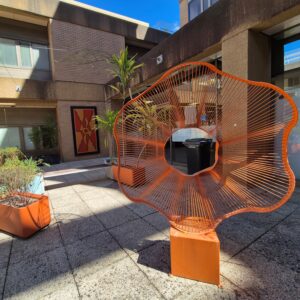 A large orange flower sculpture in a courtyard containing plants in planter boxes.