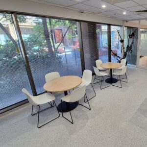 Modern tables and chairs beside floor-to-ceiling windows that look out on to a green courtyard.