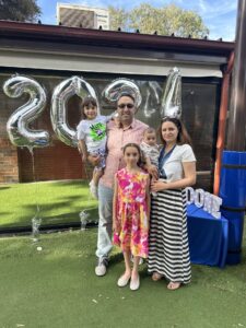 Three young children pose for a photo with their parents at a celebration.