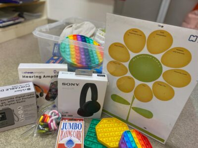 Delirium toolkit box, containing various items including fidget toys, playing cards and hearing amplifiers.