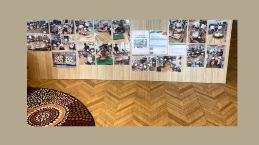 At Community Kids Narre Warren, the reception area proudly showcases vibrant images of children joyfully engaging in cooking and food education activities, highlighting the fun and positive experiences happening in the classroom.