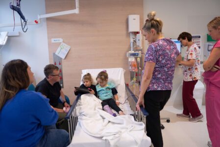 A six-year-old patient in a hospital bed. He sister and parents and three nurses watch on.