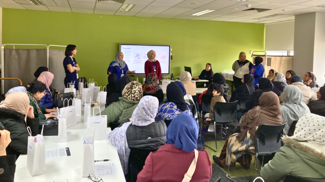 A group of women wearing headscarves listen attentively to a woman giving a presentation.