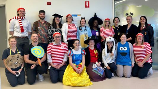 A large group of adults in fancy dress. Costumes include Snow White, Hogwarts school uniform, and Wally from Where's Wally?