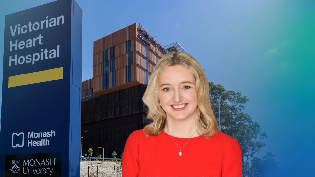 A smiling woman wearing a bright red dress. Behind her is the exterior of a hospital and a sign reading 'Victorian Heart Hospital'.