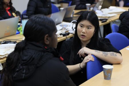 Photo of a Deadly Coders instructor talking to a student who's sitting at a table.