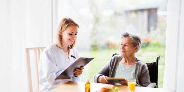 Health visitor and a senior woman with tablet. Health visitor and a senior woman with tablet during home visit. A nurse making notes.