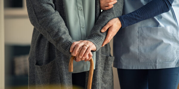 Nurse assisting senior with walking cane Close up hands of caregiver doctor helping old woman at private clinic. Close up of hands of nurse holding a senior patient with walking stick. Elder woman using walking cane at nursing home with nurse holding hand for support.