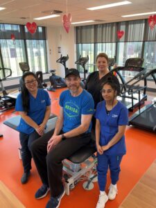 Alex in the rehab gym with three health workers around him, all smiling at the camera