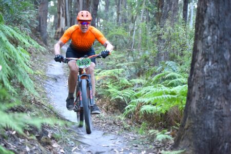 Alex riding a mountain bike fast downhill on a rainforest trail.