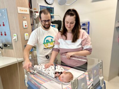 A new mum and dad standing at the side of a hospital bassinet looking down on the sleeping baby son.