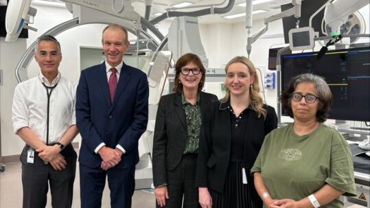 Cardiologists, the Health Minsiter and a patient standing in a cath lab in the Victorian Heart Hospital