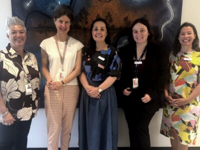 The 5 members of the PTGH Southern Melbourne stand in front of an Indigenous Australian artwork.